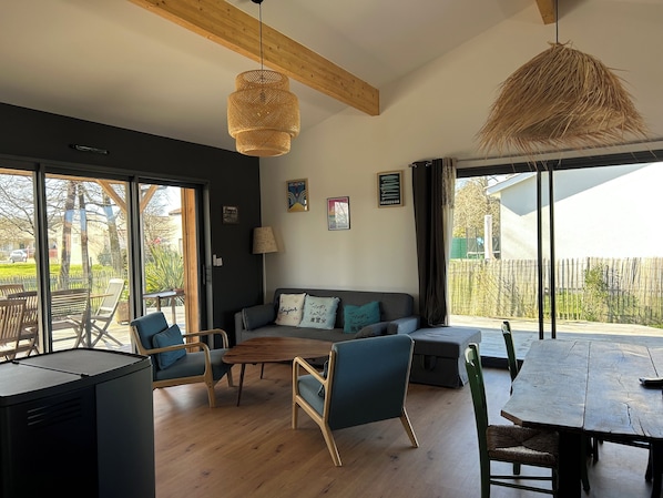 Un salon moderne comprenant un canapé, des fauteuils, une table basse en bois et une table à manger. Une grande fenêtre offre une vue sur l’extérieur.