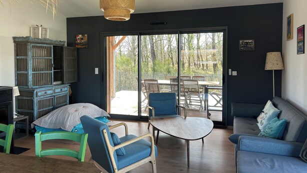 Una sala de estar moderna con un amplio ventanal corredera que da a un patio exterior, un sofá azul, un sillón verde y una mesita.