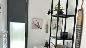 Un baño pequeño con un lavamanos blanco, estantería negra y una ventana con vidrio esmerilado.