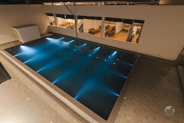 Una piscina interior moderna con agua cristalina, rodeada por un diseño minimalista y un área de estar con sillas y mesas.