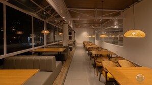 A modern restaurant with high ceilings, exposed beams, and large windows offering views of the city at night. - COUNTRYSIDE RESORT MURTI (Mal)
