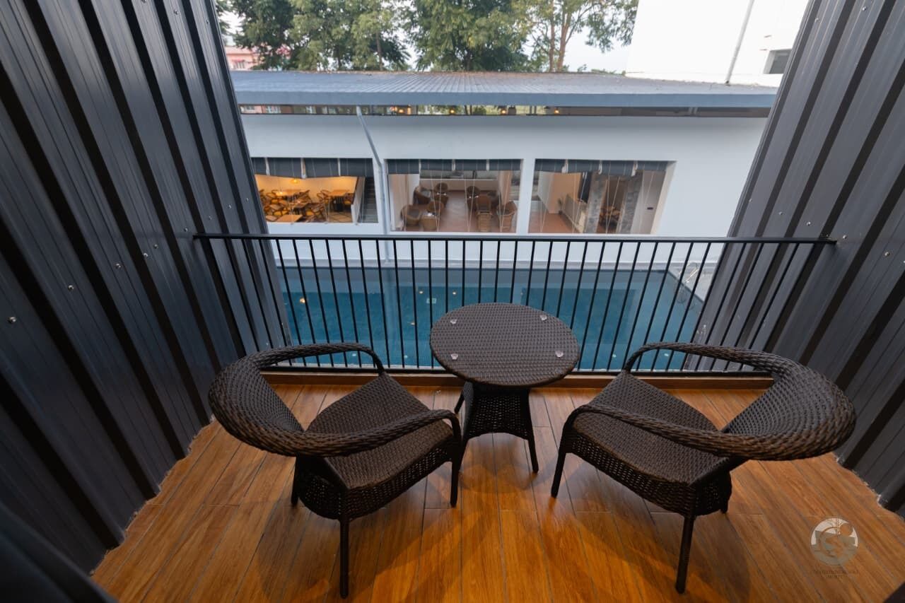 A balcony with wicker furniture and a view of a swimming pool and building.