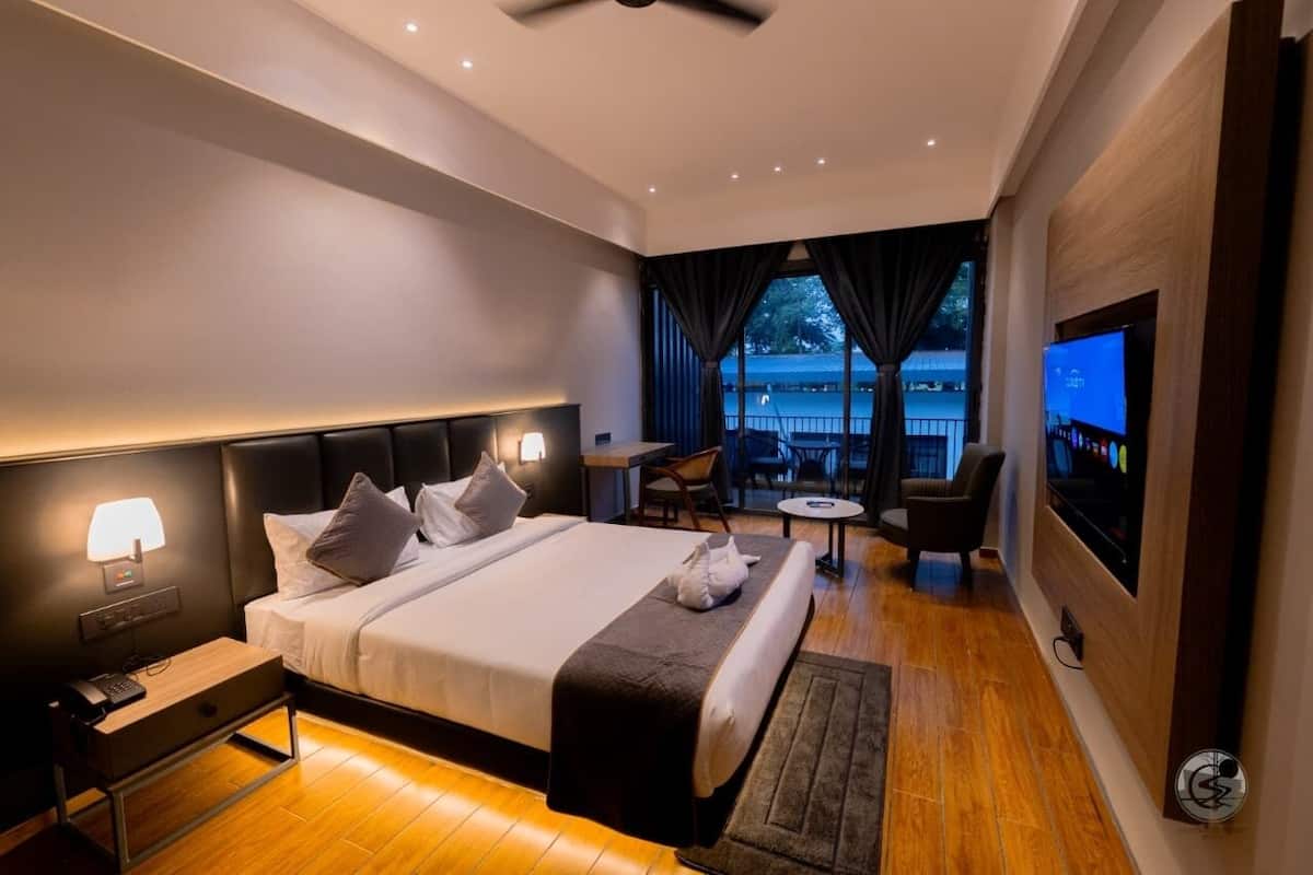 Habitación de hotel moderna con una cama grande, mesitas de noche, un escritorio, una silla, un televisor y un balcón con vistas.