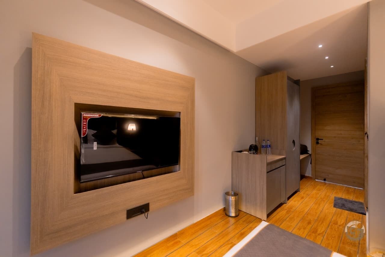 A modern kitchen with wooden cabinets, a built-in TV, and a small trash can.