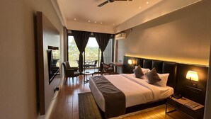 A modern hotel room with a large bed, a ceiling fan, a TV, a desk, and a balcony with a view. - COUNTRYSIDE RESORT MURTI (Mal)
