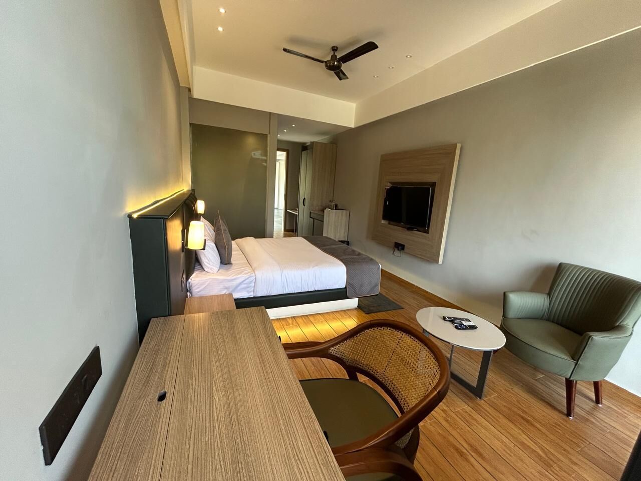 A hotel room with a bed, a desk, a chair, a sofa, a TV, and a ceiling fan.