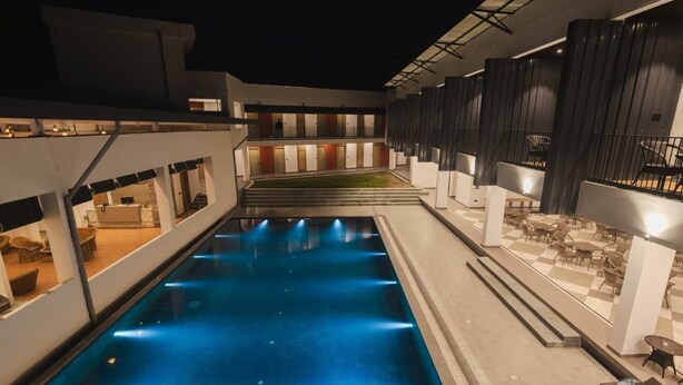A swimming pool with steps leading to a covered area, surrounded by modern architecture and outdoor seating. - COUNTRYSIDE RESORT MURTI (Mal)