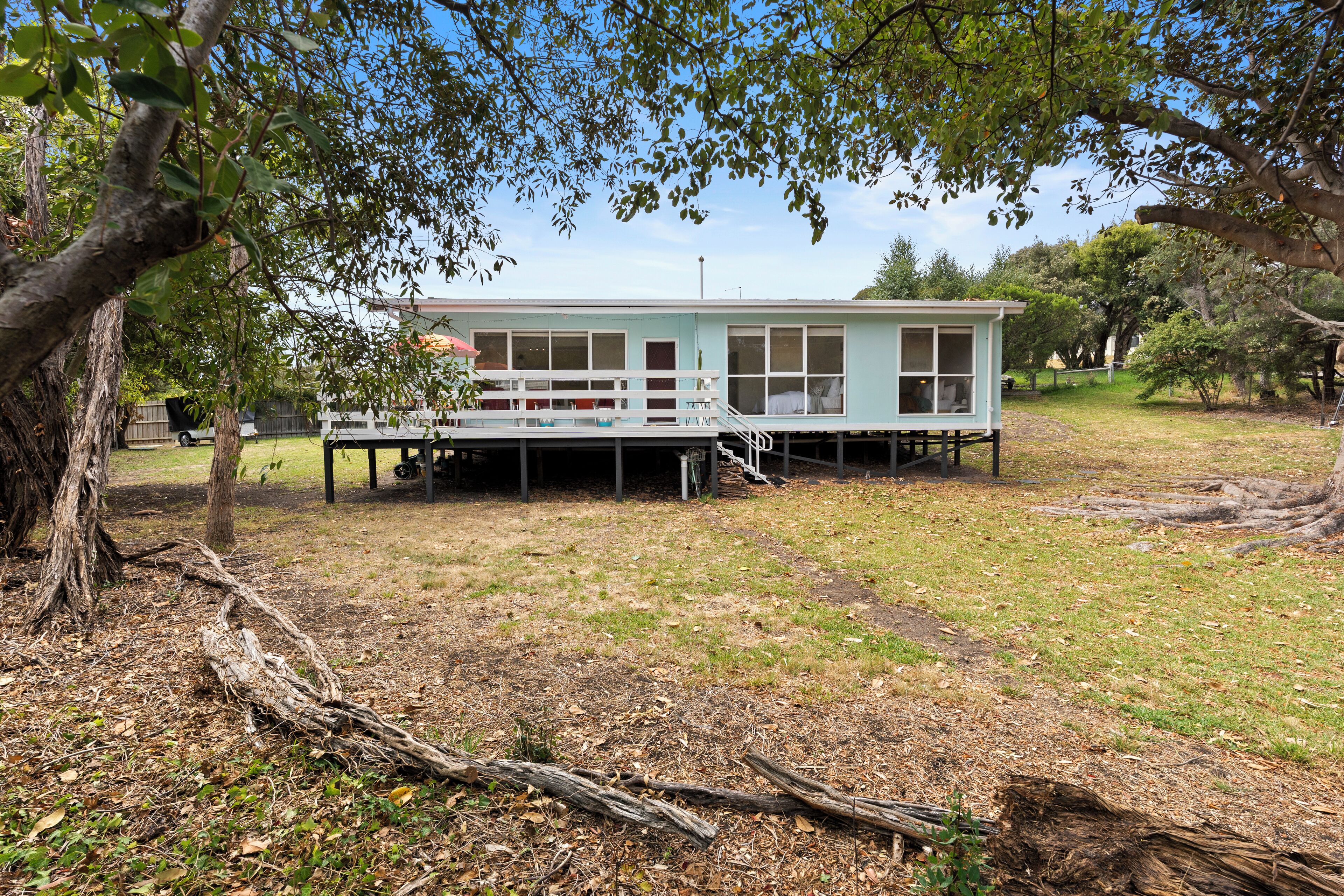 A single-story house with a porch, surrounded by trees and grass.