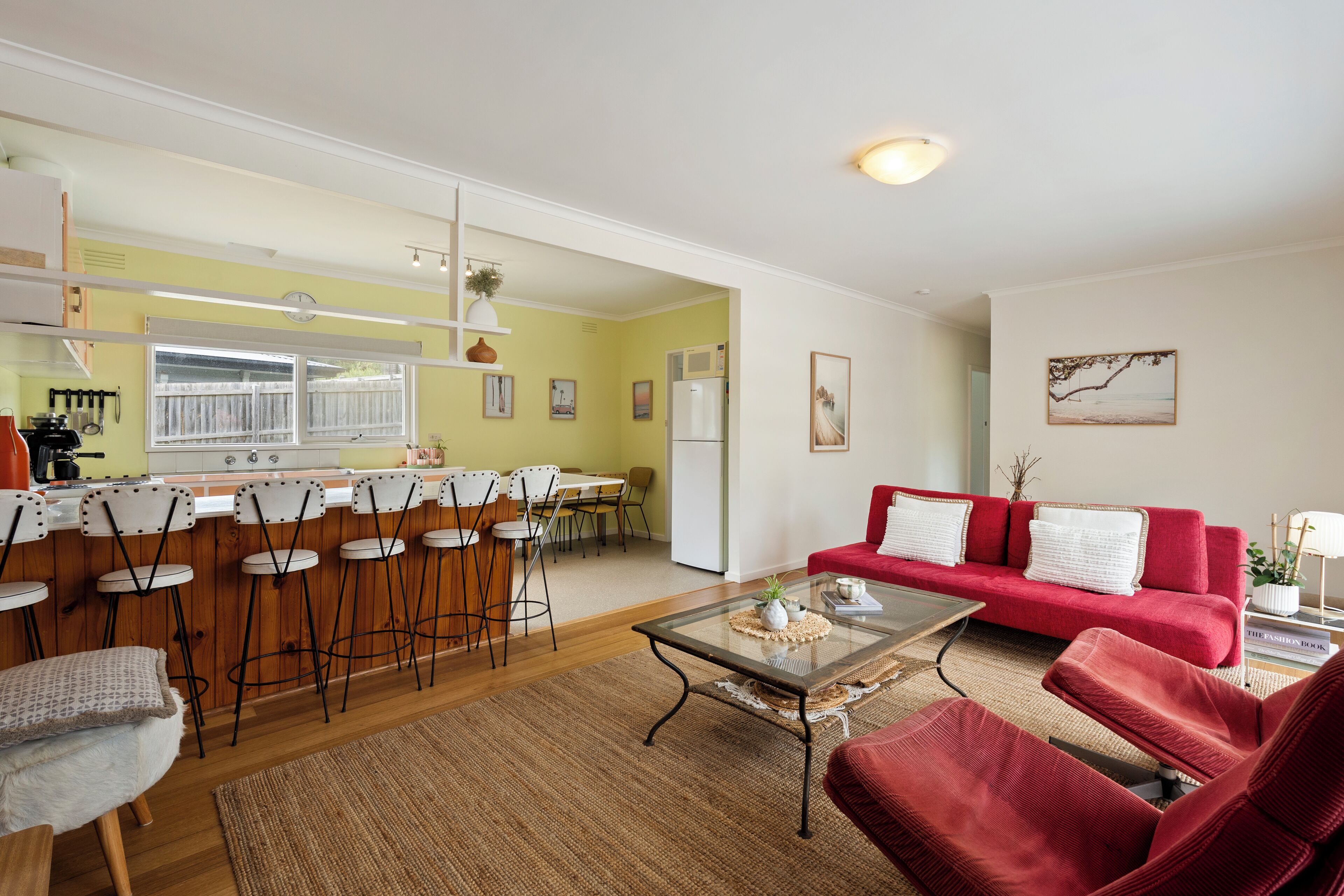 A spacious living area with a red sofa, a glass coffee table, and a kitchen in the background.