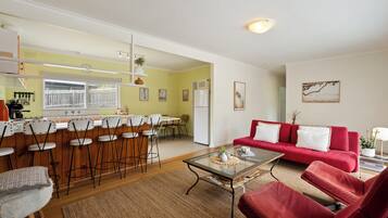 A spacious living area with a red sofa, a glass coffee table, and a kitchen in the background.