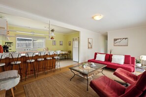 A spacious living area with a red sofa, a glass coffee table, and a kitchen in the background. - Retro Charlies Beach House (Rye)