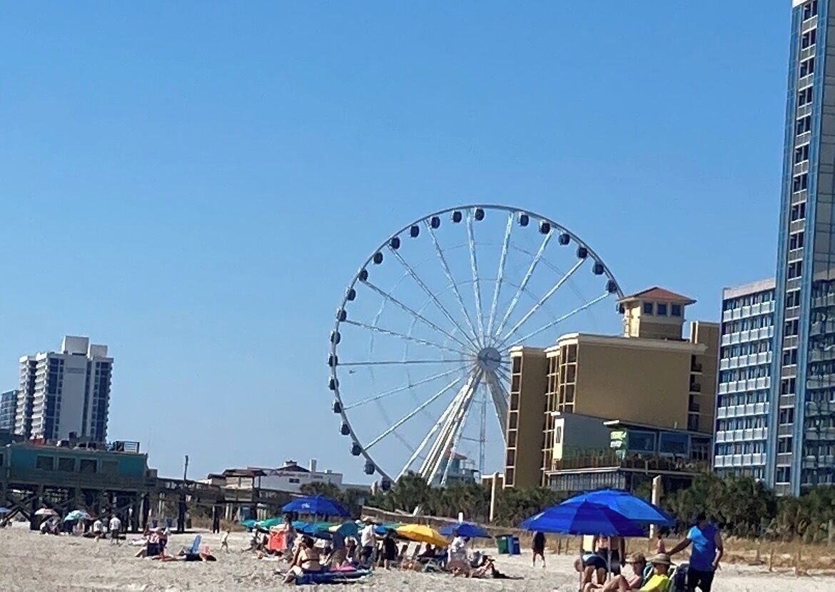 Une plage avec une grande grande roue en arrière-plan, entourée de bâtiments et de parasols.