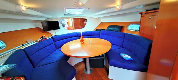 A compact, well-lit interior with a round table, blue cushioned seating, a television, and a wooden cabinet.