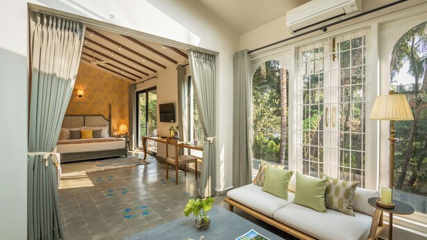 A spacious room with a large window, a sofa, a dining area, and a bed. - TBK Villa Calangute (Calangute)