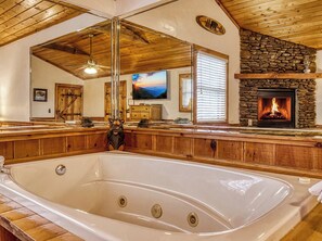 A large wooden bathtub in a room with a stone fireplace, wooden ceiling beams, and a television on the wall. - 8 minutes from Pigeon Forge Tn/ Hot Tub/Jacuzzi Tub/ Wifi (Sevierville)