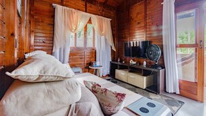 A wooden cabin room with a bed, a TV, a fan, and a window with curtains. - Casa p 5 Pessoas Perto das Praias e Beto Carrero (Penha)