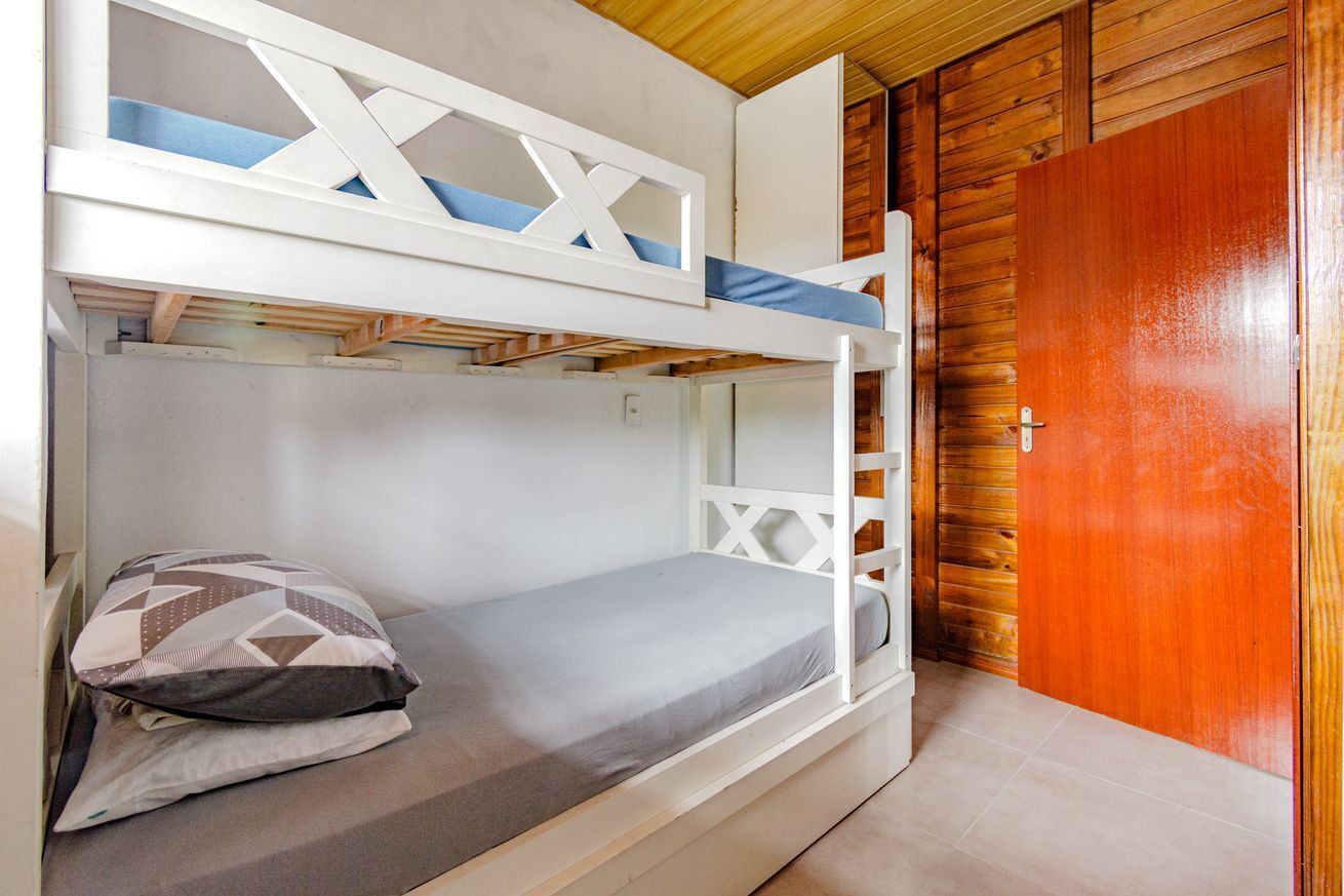 A bunk bed with a wooden ladder, a single bed with a pillow, and a wooden door.