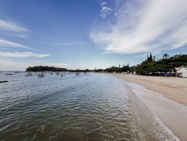 Une plage aux eaux calmes, un rivage sablonneux et une petite île qui se dessine à l’horizon.