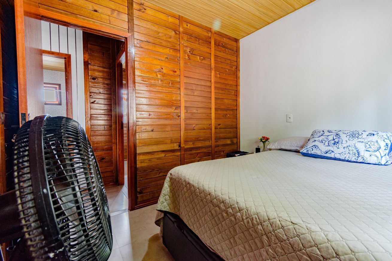 A bedroom with a wooden ceiling, a bed with a quilted cover, a nightstand with a lamp, and a wooden wardrobe.