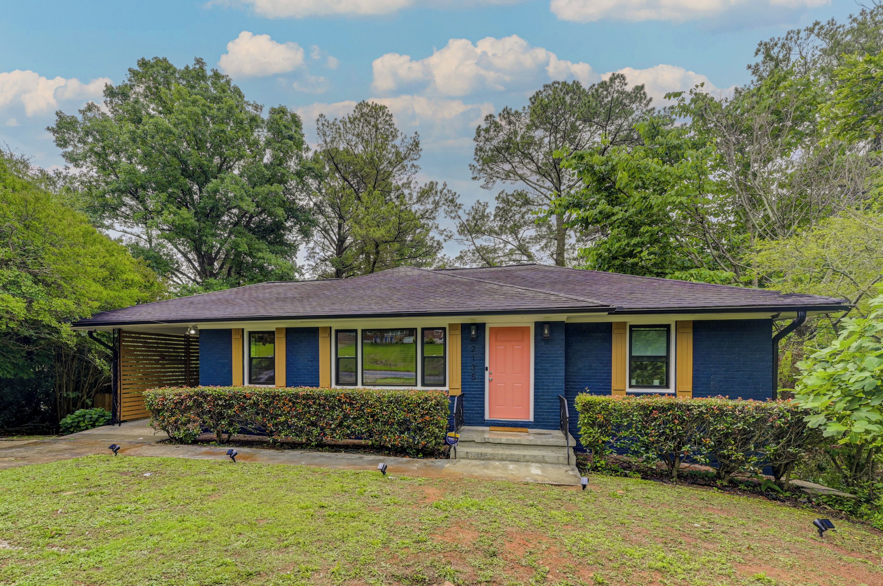 A single-story house with a dark blue exterior, yellow trim, and a red door.