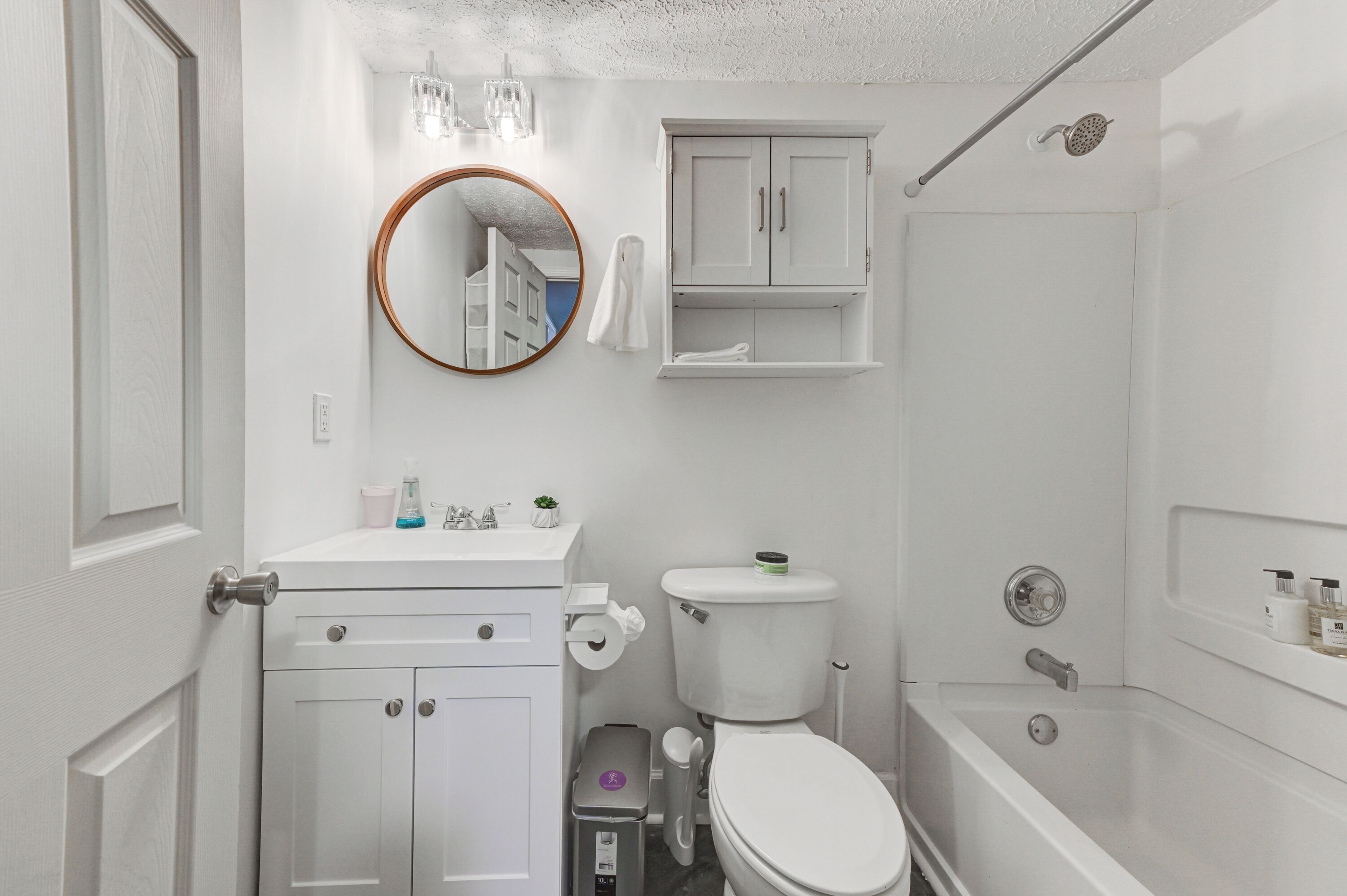 A bathroom with a toilet, sink, mirror, cabinet, and shower.