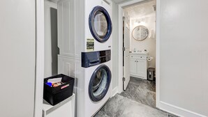 A laundry room with a front-loading washer and dryer, a black basket with items, and a small trash can. - Boutique ATL Escape Movie Room and Covered Deck (Atlanta)