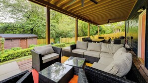 An outdoor covered patio with wicker furniture, a ceiling fan, and a view of a wooded area. - Boutique ATL Escape Movie Room and Covered Deck (Atlanta)