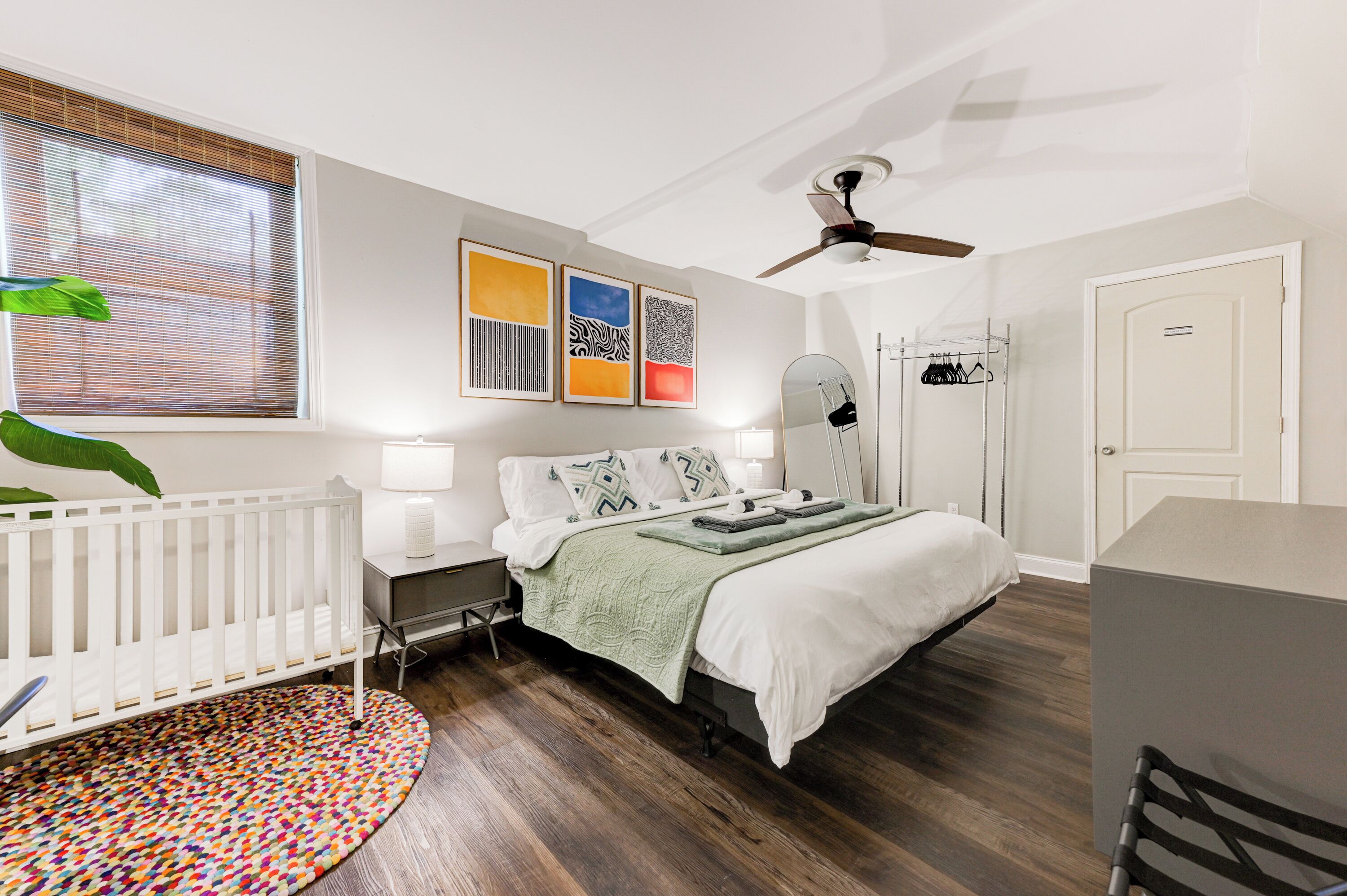 A bedroom with a bed, bedside table, lamp, ceiling fan, and a window with blinds.