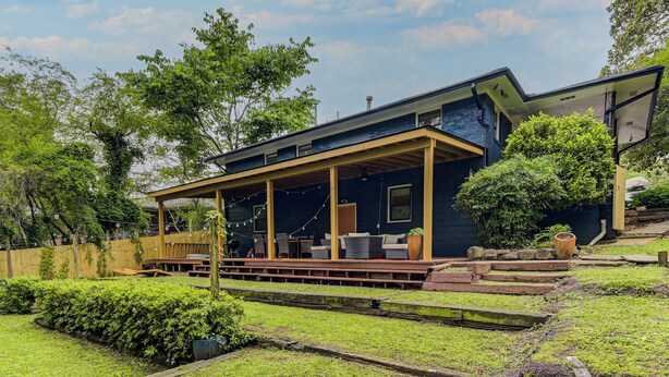 A modern house with a covered porch, a wooden deck, and a well-maintained garden. - Boutique ATL Escape Movie Room and Covered Deck (Atlanta)