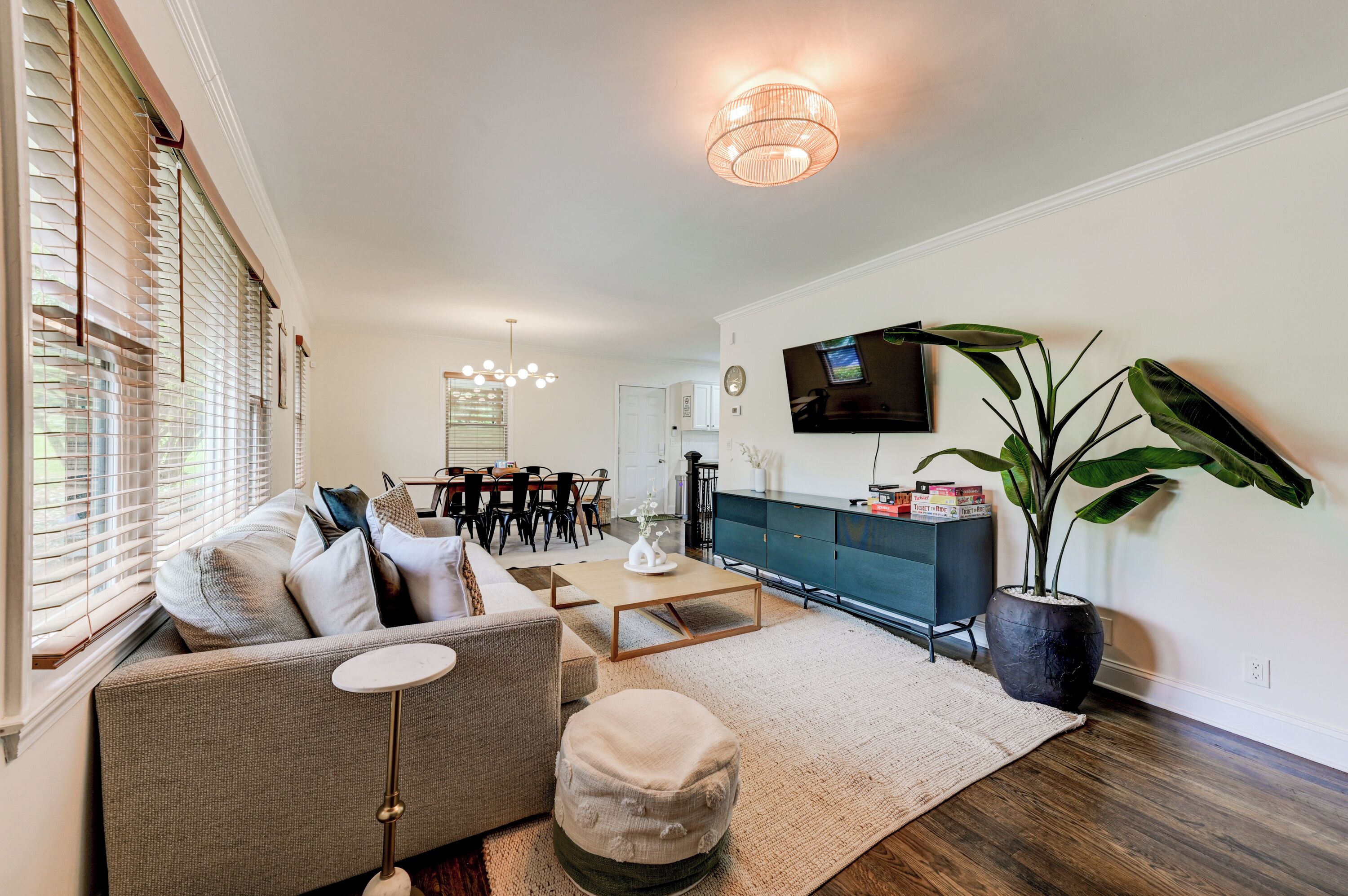 A living room with a sofa, coffee table, ottoman, dining area, TV, and a large plant.
