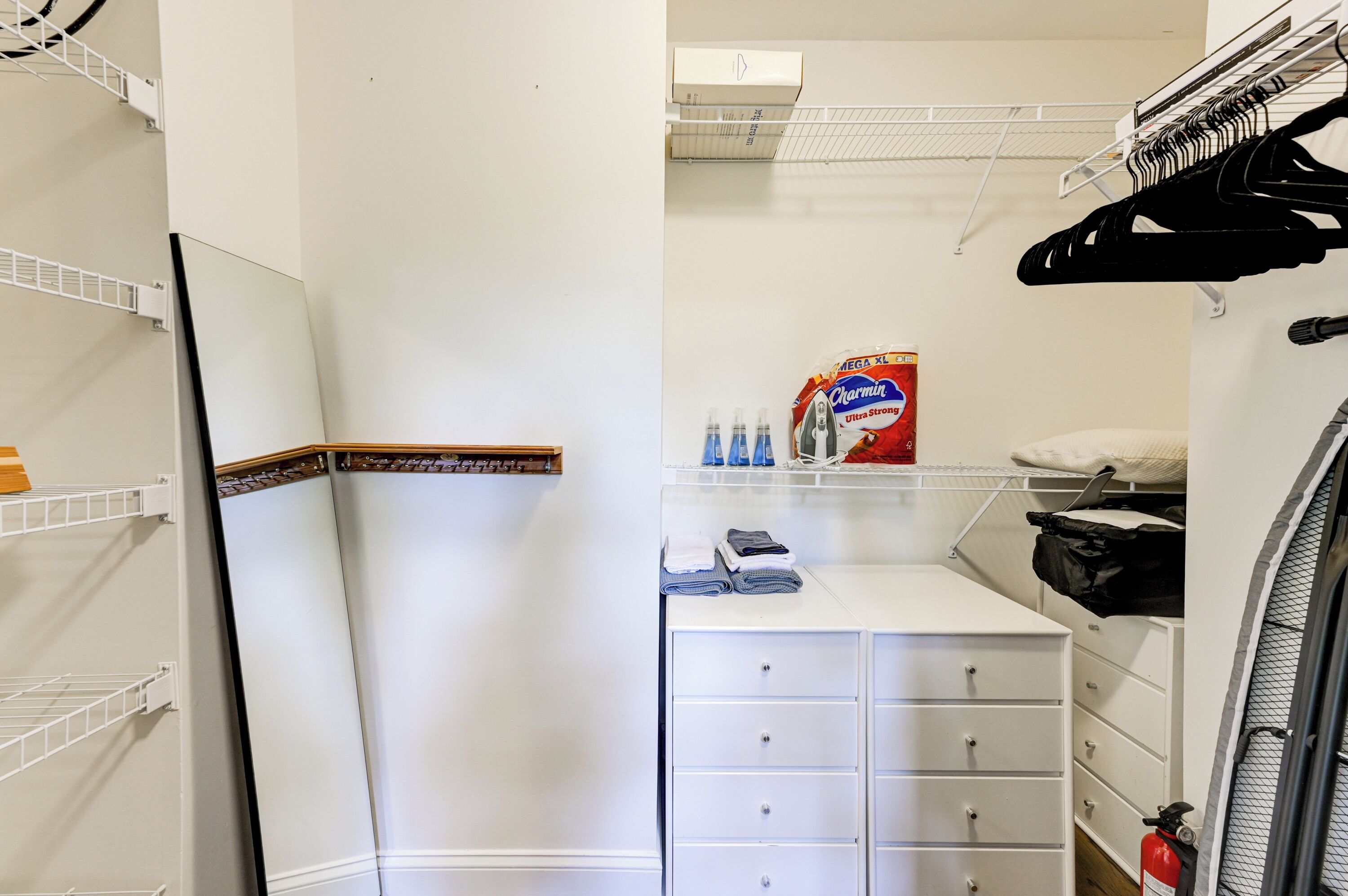 Ein kleines Hotelzimmer mit weißem Kleiderschrank, einem Tisch mit Pflegeartikeln, einer Kleiderstange und einer weißen Heizung.