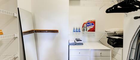A compact hotel room with a white wardrobe, a small table with toiletries, a hanging clothes rack, and a white radiator.