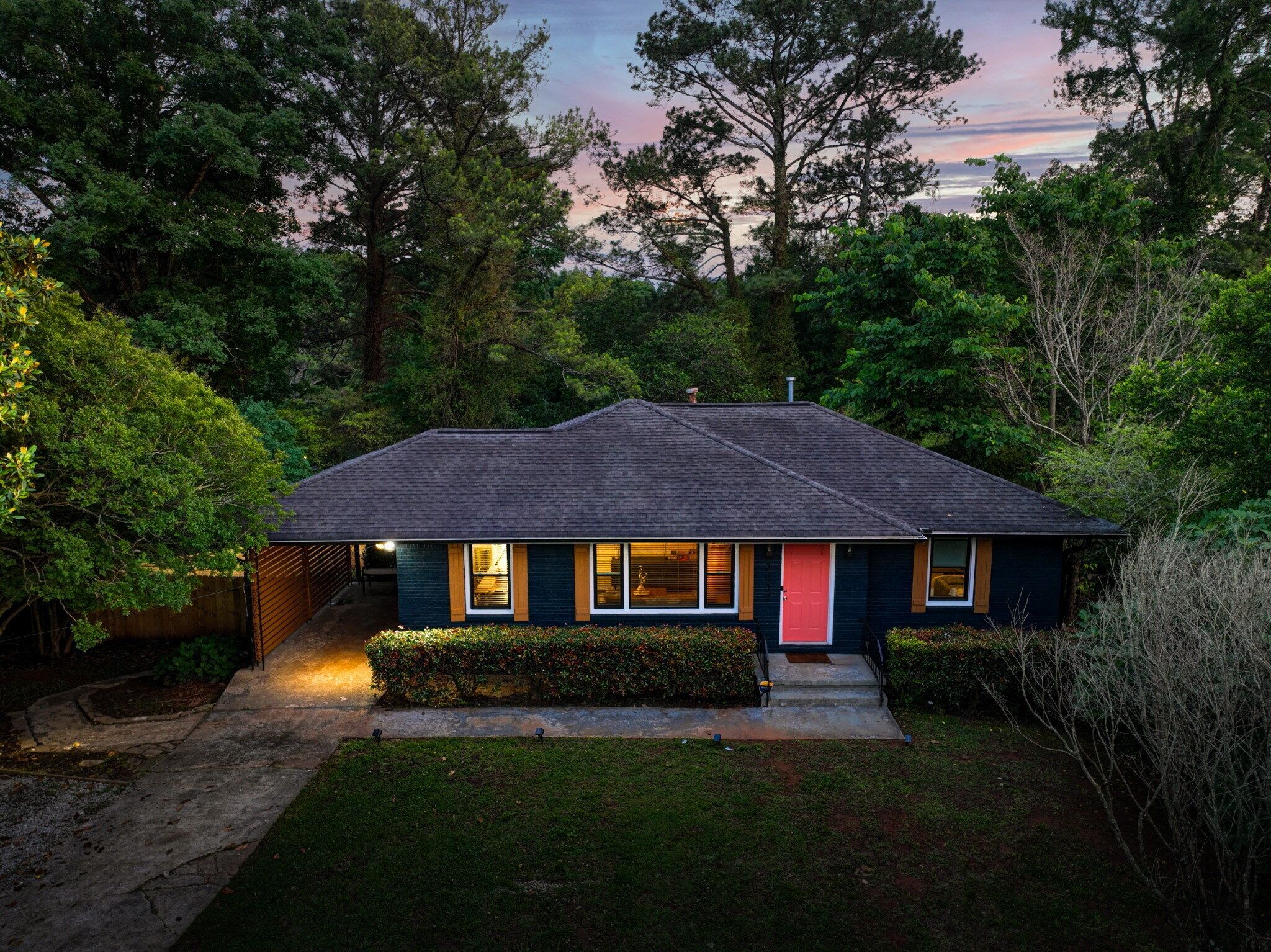A single-story house with a dark roof, a red door, and a well-lit front yard.