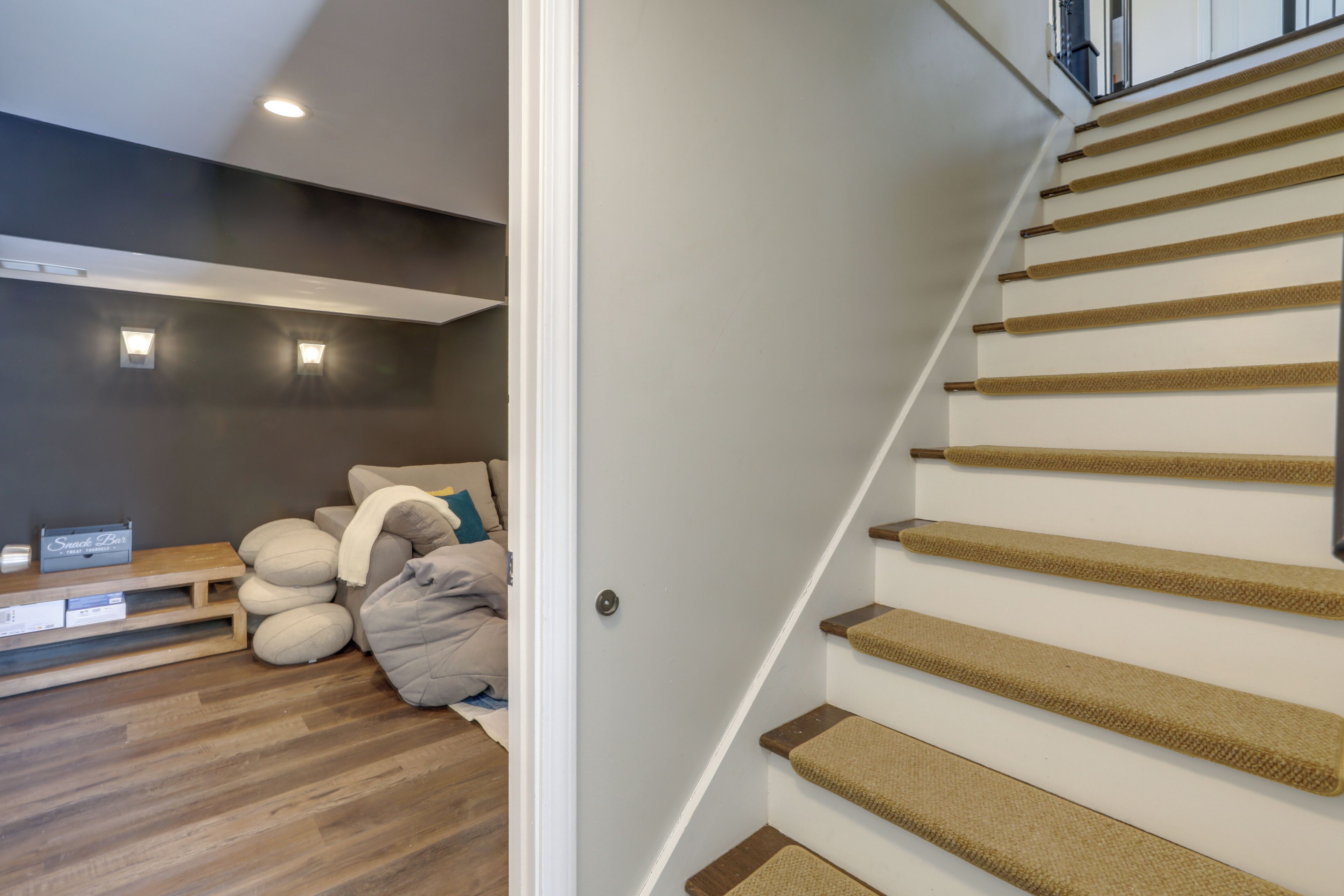 A staircase with a wooden handrail and carpeted steps, leading to a landing with a sofa and pillows.