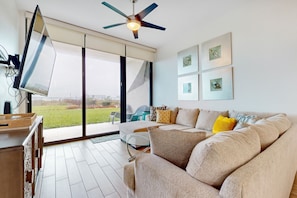 Ein modernes Wohnzimmer mit einer großen Couch, einem Flachbildfernseher und einem Deckenventilator.