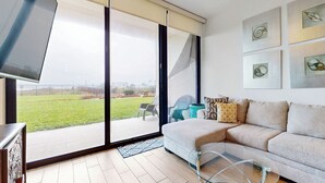 Ein modernes Wohnzimmer mit einem Glastisch, einem beigefarbenen Sofa und einem großen Schiebeglastür, die auf einen Balkon führt.