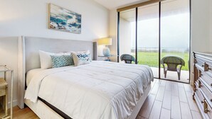 Ein Schlafzimmer mit einem großen Bett, einem Deckenventilator, einem Nachttisch mit Lampe und Blick ins Freie durch eine Schiebetür.