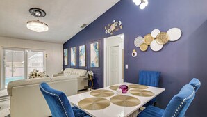A dining area with a white table, blue upholstered chairs, and decorative wall art. - 5 Mi to Disney: Renovated Group Getaway, Game Room (Kissimmee)