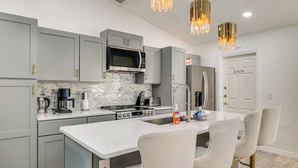 A modern kitchen with grey cabinets, a central island, stainless steel appliances, and a white countertop. - 5 Mi to Disney: Renovated Group Getaway, Game Room (Kissimmee)