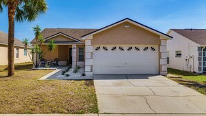 A single-story house with a garage, a covered patio, and a lawn with palm trees. - 5 Mi to Disney: Renovated Group Getaway, Game Room (Kissimmee)