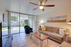 A spacious living room with a sliding glass door leading to a patio, a ceiling fan, a sofa, a coffee table, and a lamp. - Walk to Waterfront! Couples Retreat in Old Town (Scottsdale)