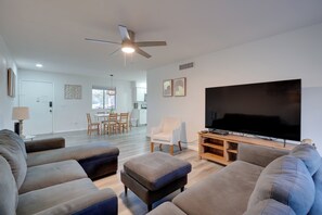 Uma sala de estar moderna com uma grande TV de tela plana, um ventilador de teto e uma área de jantar ao fundo.
