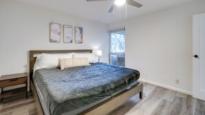 Een slaapkamer met een bed, nachtkastje, plafondventilator en raam met uitzicht.