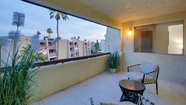 Een balkon met uitzicht op palmbomen en gebouwen, een plant in pot en een tafel met stoelen.