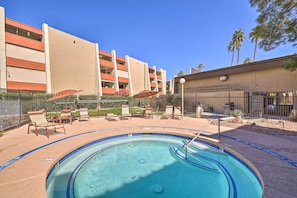 A swimming pool with lounge chairs and umbrellas, surrounded by a fence and a building with multiple balconies. - Old Town Oasis! Modern Unit w/ Resort-style Pool (Scottsdale)