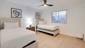Een slaapkamer met twee bedden, een plafondventilator en kunstwerken aan de muur.