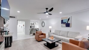 Een moderne woonkamer met een bank, fauteuils, een salontafel en een eethoek op de achtergrond.