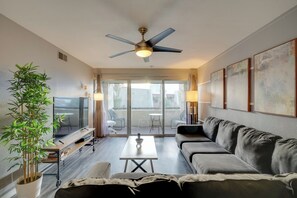 A modern living room with a sofa, a coffee table, a TV, and a ceiling fan. There is a sliding glass door leading to an outdoor area with chairs. - Fully Renovated! Walkable Old Town Condo (Scottsdale)