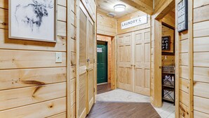 A wooden interior hallway with a framed animal painting, a laundry sign, and a cold nose warm heart sign. - Waterfall Log Cabin: Private Hot Tub & Game Room (Gatlinburg)