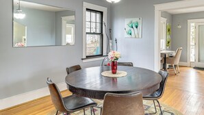 A dining area with a round table, six chairs, a vase with flowers, and a large mirror on the wall. - Lakeside Clifton Heights Home Near Forest Park (St. Louis)